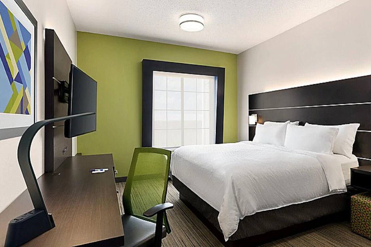 A hotel room with a bed, a desk, a chair, a TV, and a window.