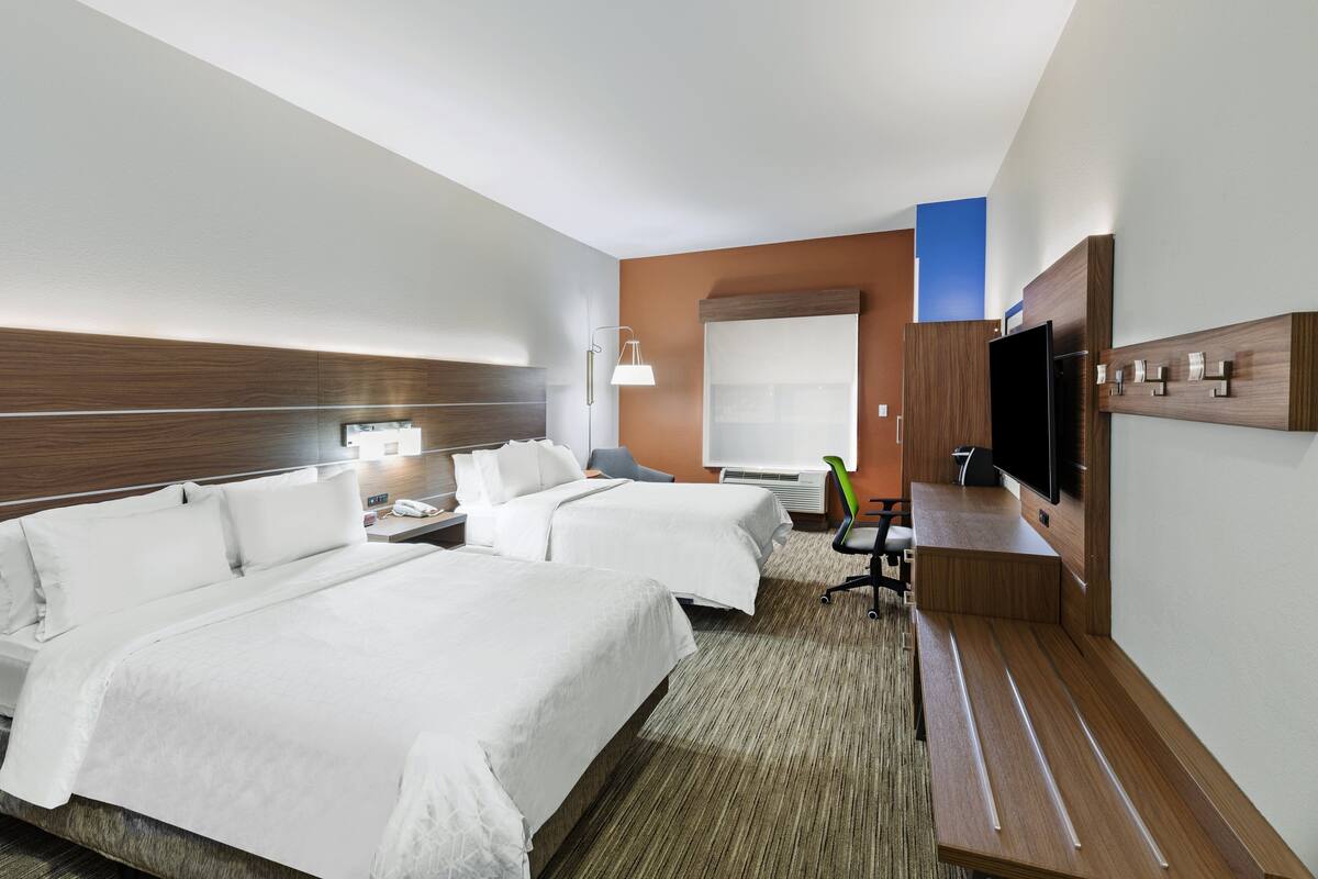 A hotel room with two beds, a desk, a chair, a television, and a window.