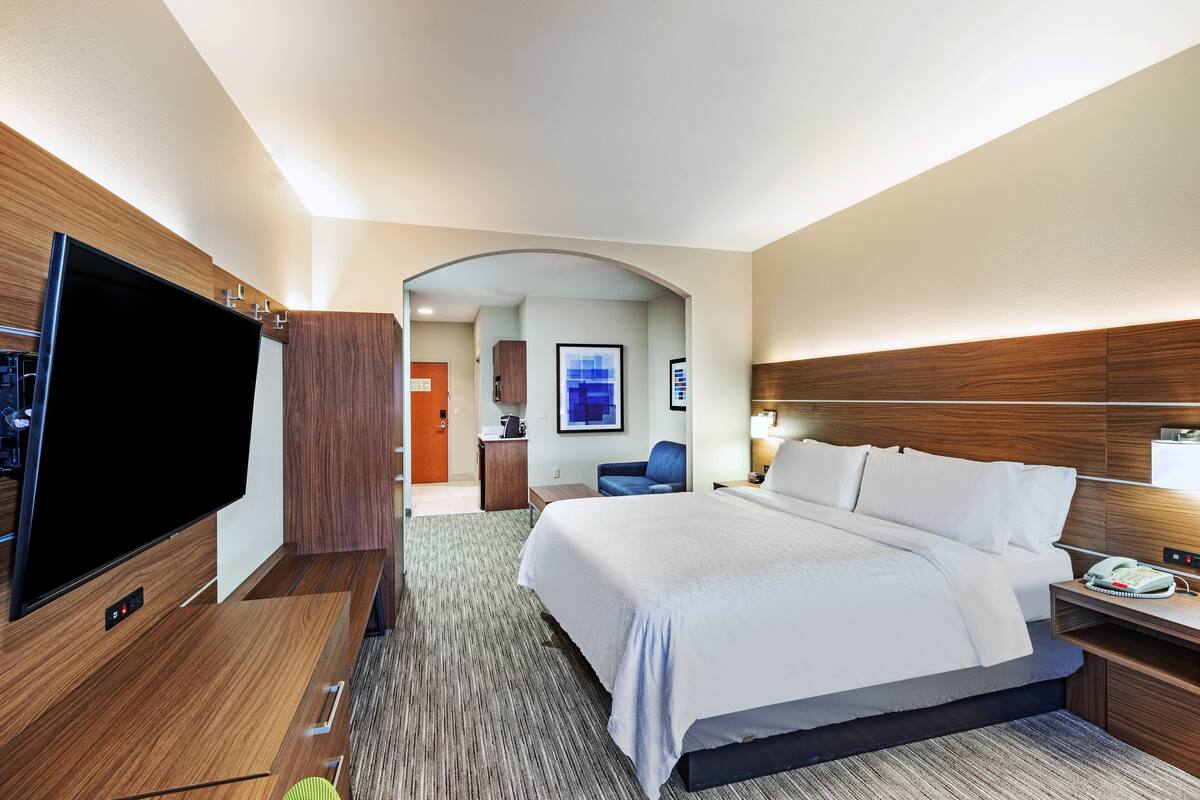 A hotel room with a large bed, a flat-screen TV, a desk with a lamp, and a wooden headboard.