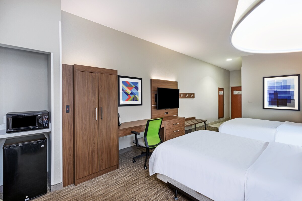 Habitación de hotel con cama, escritorio, silla, televisión, microondas y refrigerador.
