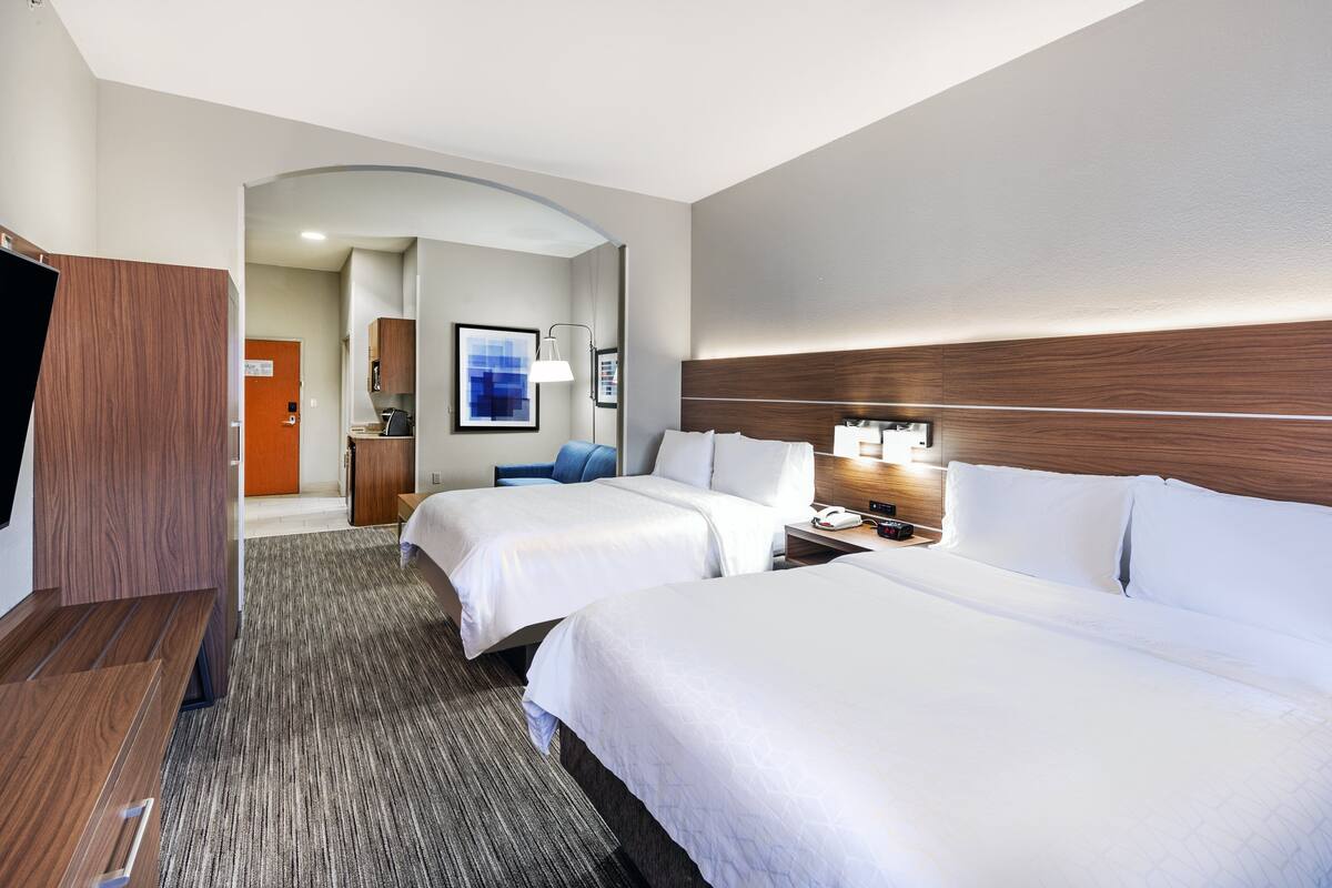 A hotel room with two beds, a desk, a chair, and a TV.