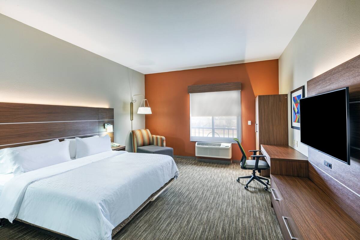 A hotel room with a bed, a desk, a chair, a TV, and a window with blinds.