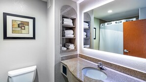 Ein Badezimmer mit einer weißen Toilette, einem Granitwaschbecken, einem großen Spiegel und Regalen mit gefalteten Handtüchern.