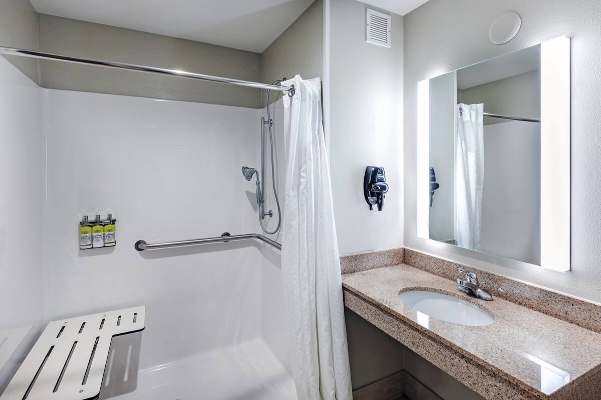A modern bathroom with a shower, grab bar, sink, and mirror.