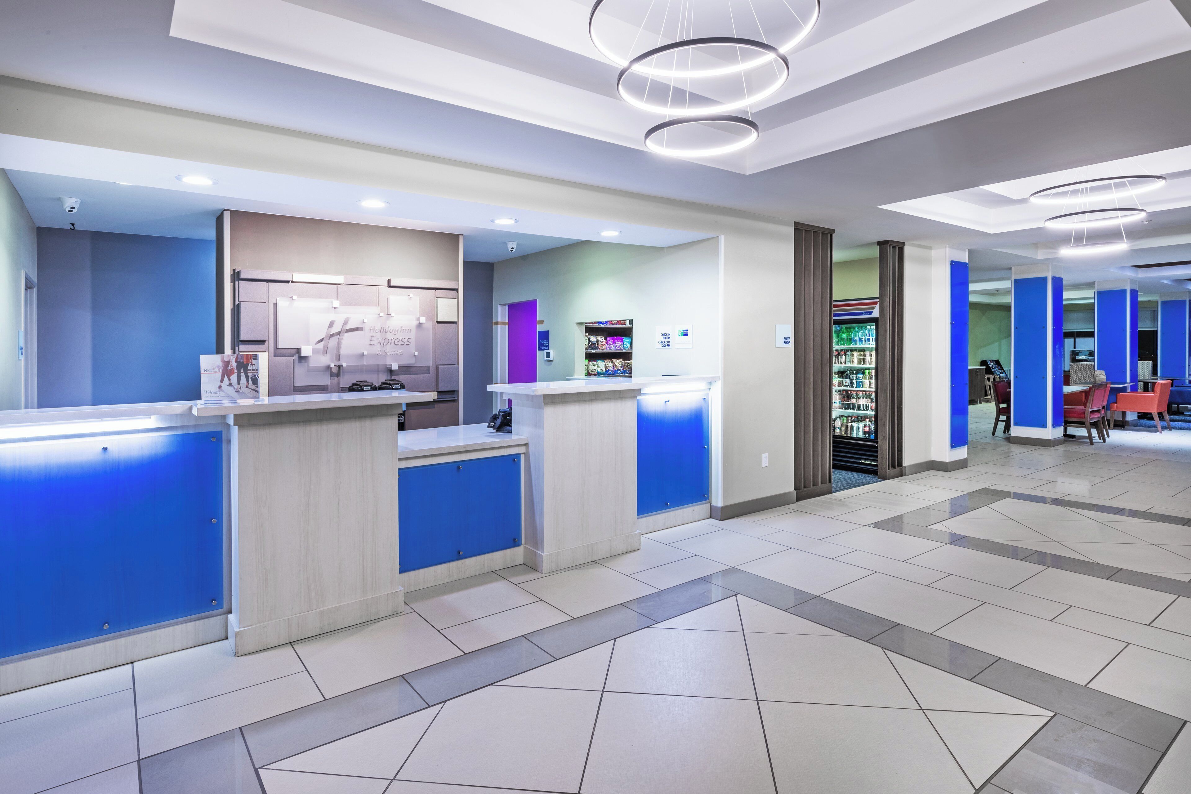 A hotel reception area with a modern design, including a reception desk, a self-service kiosk, and a seating area with tables and chairs.