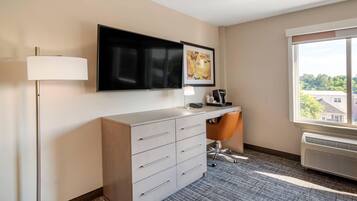 Hotelkamer met een flatscreen televisie boven een bureau, een groot raam met uitzicht op gebouwen en een vloerbedekking.