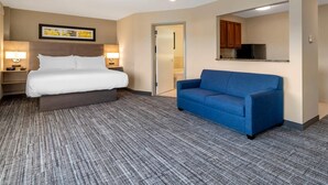 A hotel room with a bed, a blue sofa, a small desk with a lamp, a mirror, and a kitchenette. - The Inn at Leonardtown, an Ascend Collection Hotel (Leonardtown)