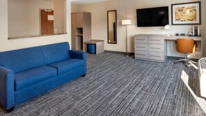A hotel room with a blue sofa, a desk with a chair, a flat-screen TV, a lamp, a coffee maker, and a framed artwork on the wall. - The Inn at Leonardtown, an Ascend Collection Hotel (Leonardtown)