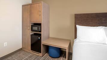 Une chambre d’hôtel avec un lit, une armoire en bois équipée d’un micro-ondes, une petite table et une poubelle bleue.