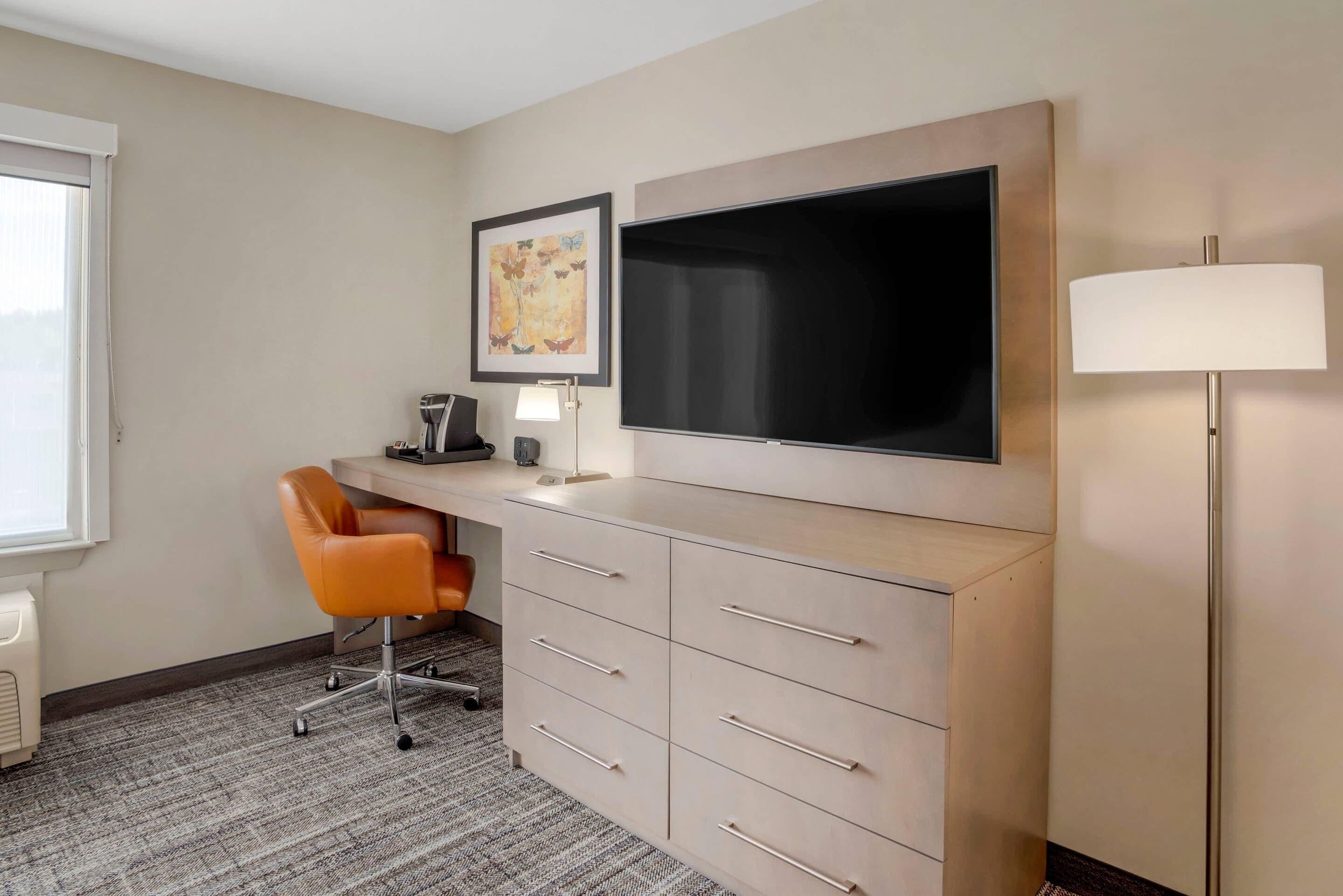 Habitación de hotel con escritorio, silla, televisor de pantalla plana y lámpara.