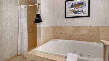 A modern bathroom with a large bathtub, a framed artwork on the wall, and a black bag hanging on a curtain rod.