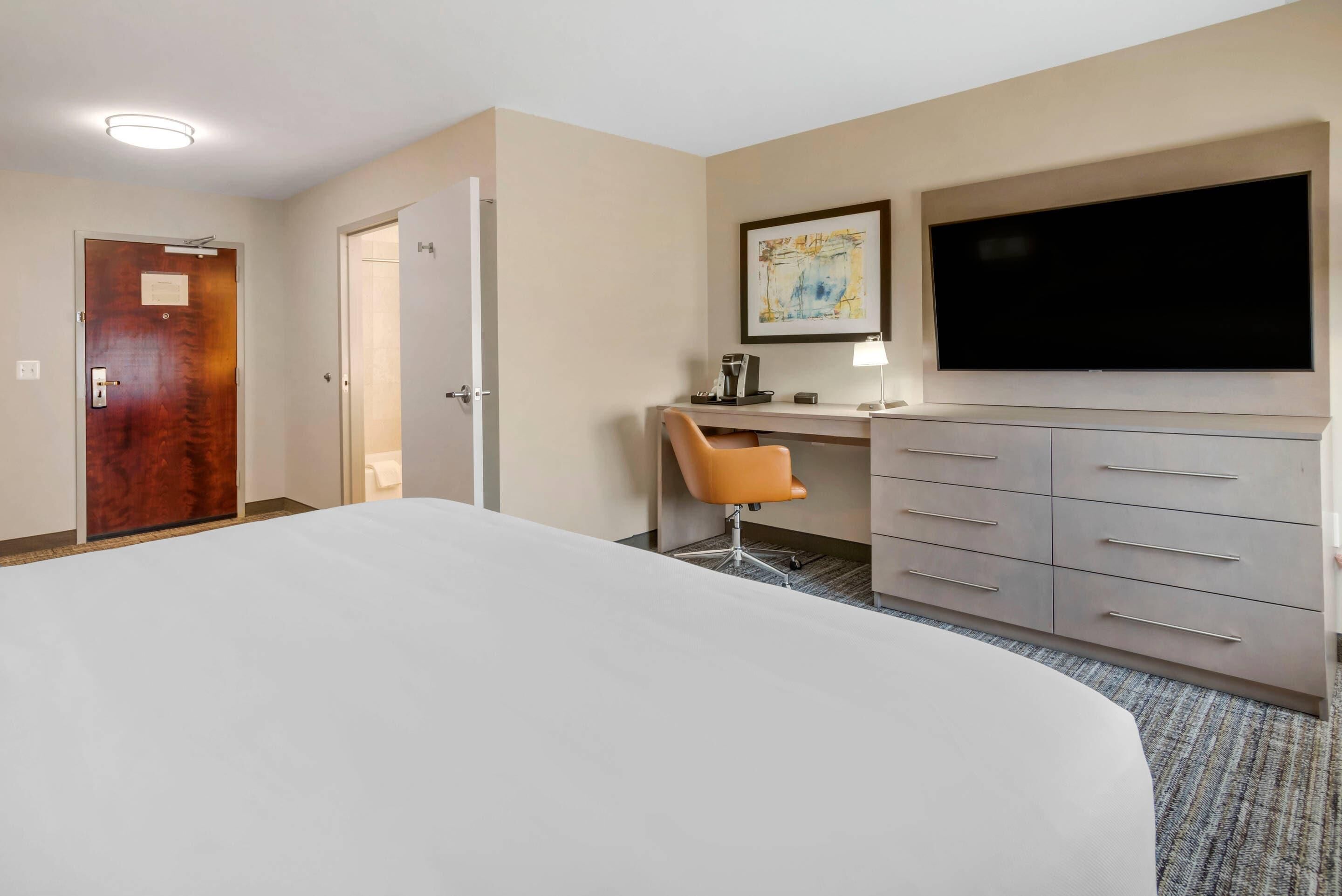 A hotel room with a large bed, a desk with a chair, a television, and a wardrobe.