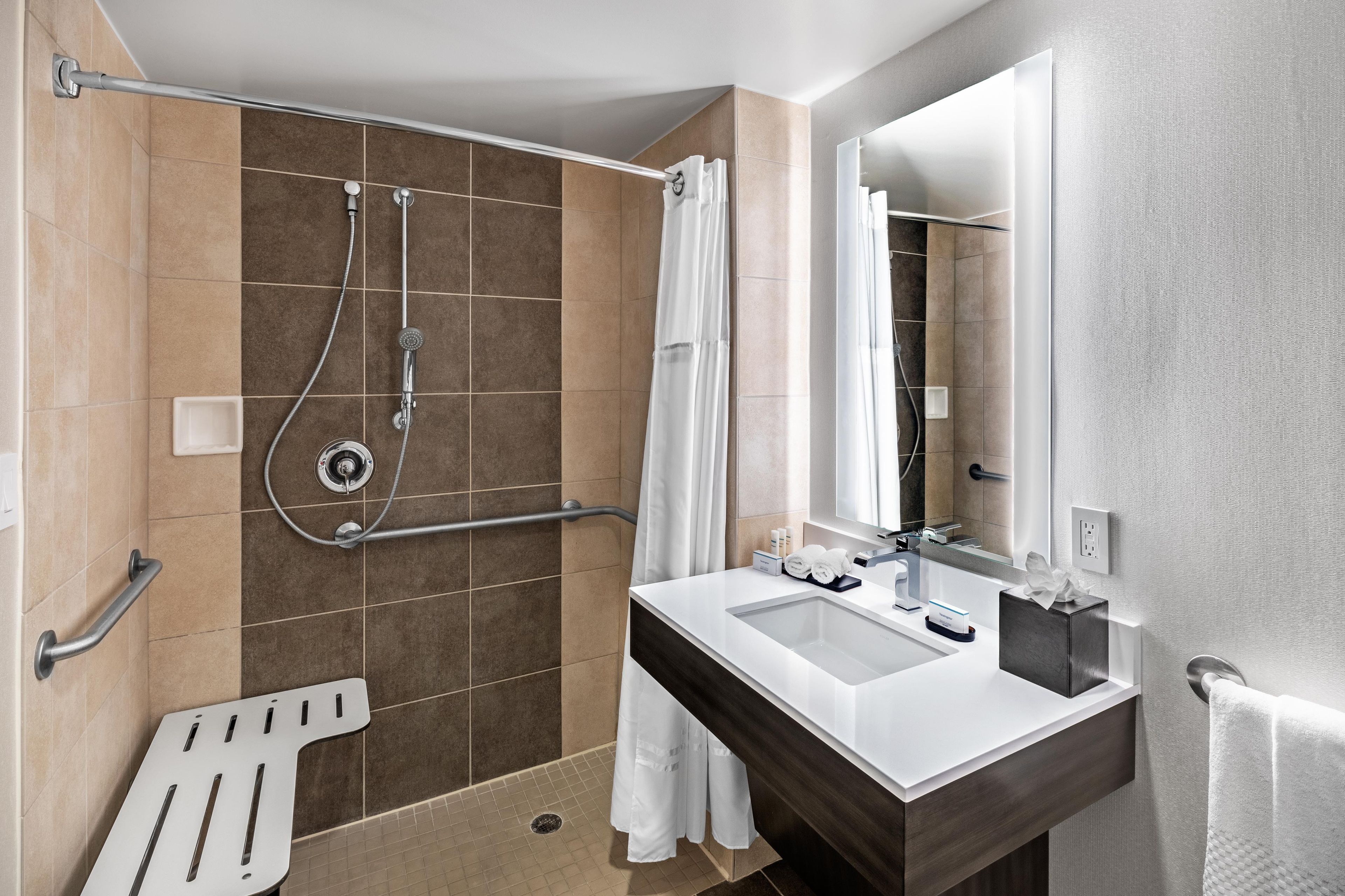 A modern bathroom with a shower, grab bar, and a sink with a mirror.
