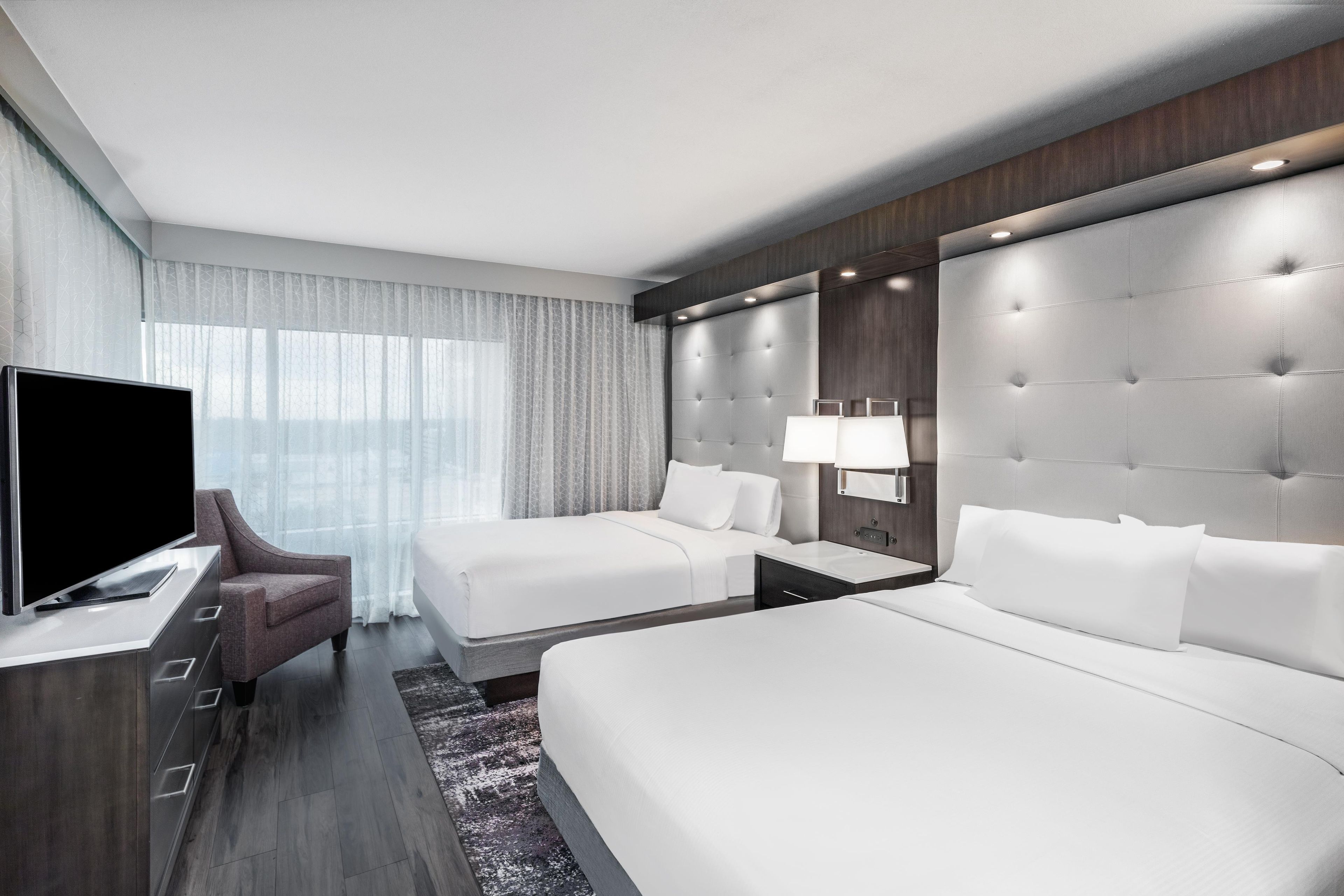 Habitación de hotel con una cama grande, una cama más pequeña, un televisor, un escritorio y una mesita de noche.