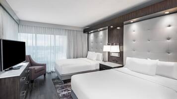 Habitación de hotel con una cama grande, una cama más pequeña, un televisor, un escritorio y una mesita de noche.