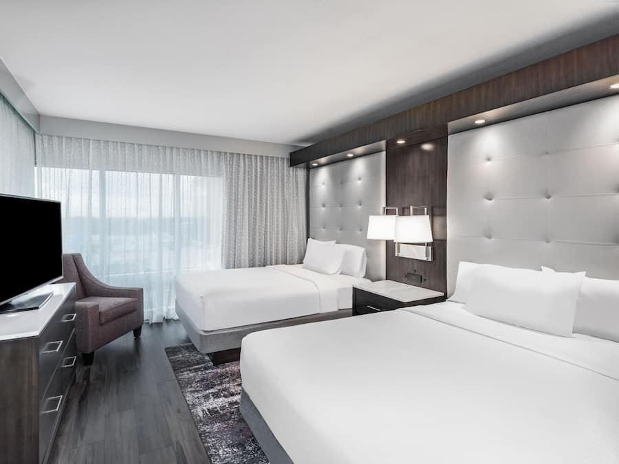 Habitación de hotel con una cama grande, una cama más pequeña, un televisor, un escritorio y una mesita de noche.