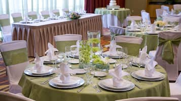 Un salón de banquetes con mesas redondas dispuestas para un evento formal, con manteles blancos, servilletas dobladas y cristalería.