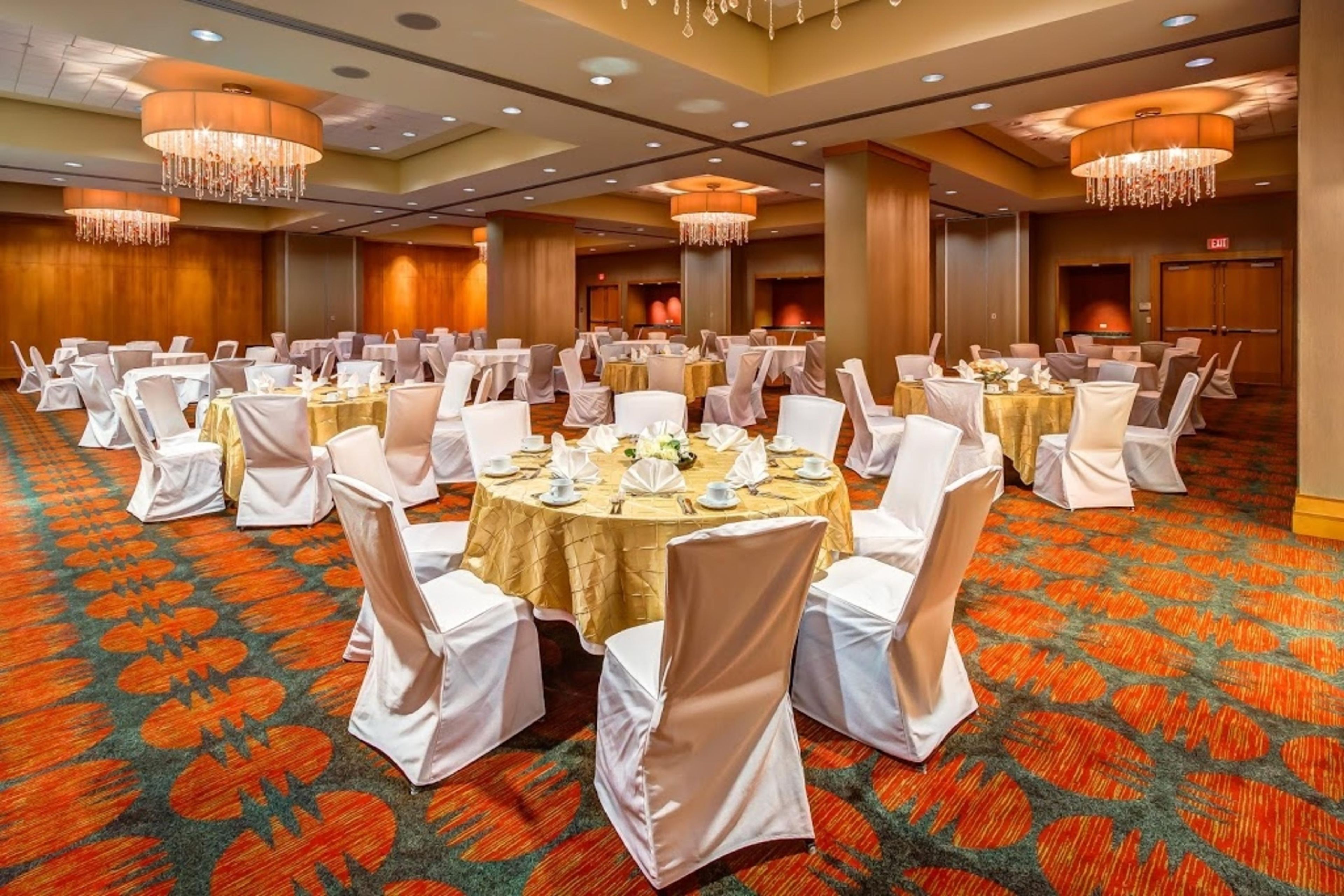 Een feestzaal met ronde tafels, witte stoelen en kroonluchters.