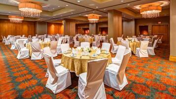 Een feestzaal met ronde tafels, witte stoelen en kroonluchters.