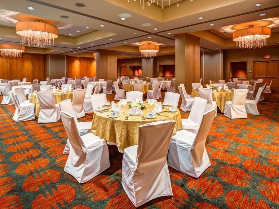 Een feestzaal met ronde tafels, witte stoelen en kroonluchters.