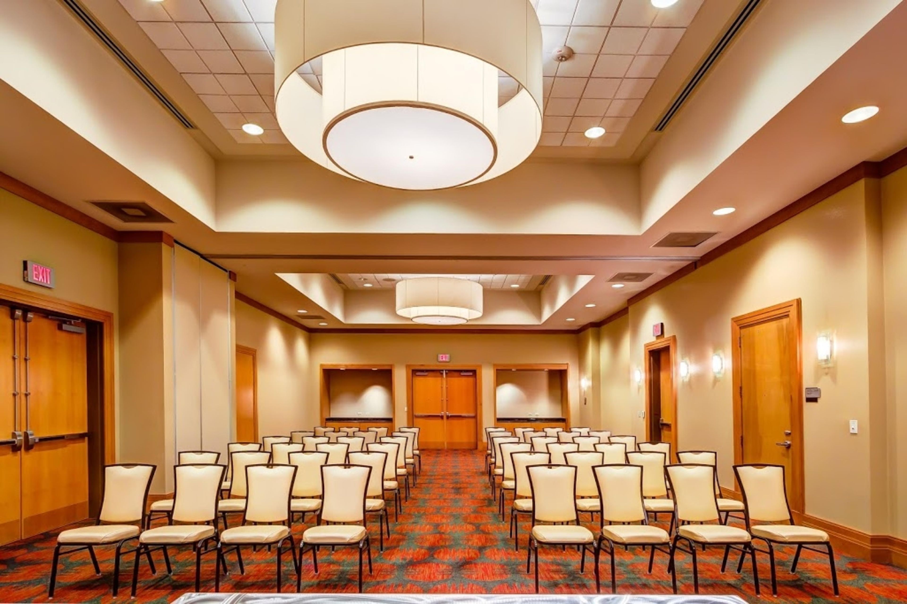 A conference room with rows of chairs, a patterned carpet, and a large circular light fixture on the ceiling.