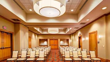 A conference room with rows of chairs, a patterned carpet, and a large circular light fixture on the ceiling.