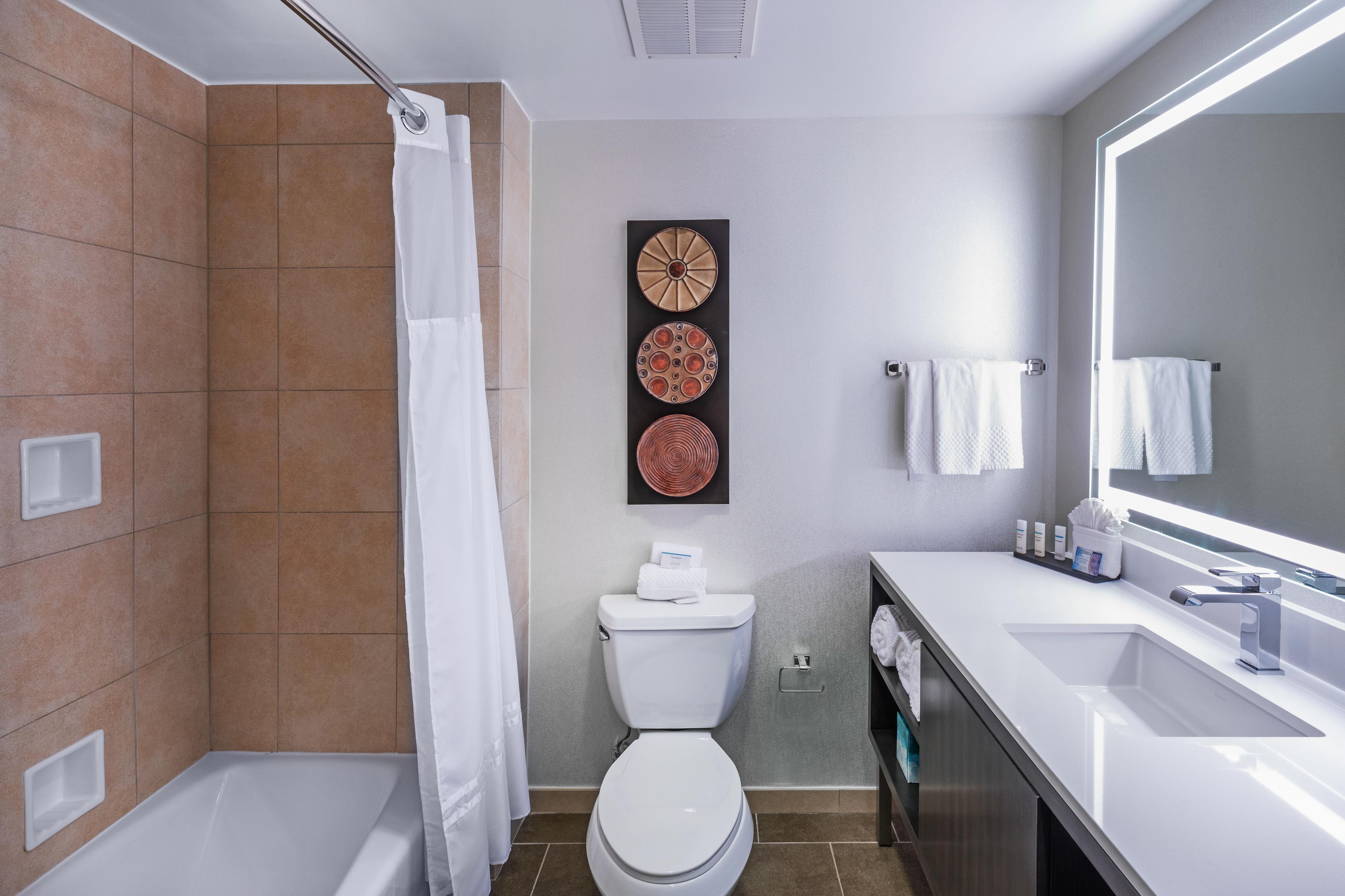 Un baño moderno con bañera, inodoro y lavamanos. Cuenta con una cortina de ducha, un perchero y un espejo.