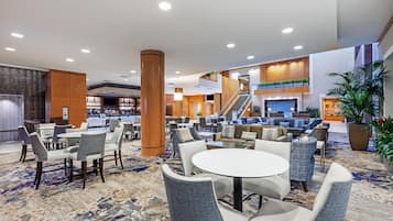 Un hall de hotel con una zona de bar, disposición de asientos y una escalera que lleva a un nivel superior.
