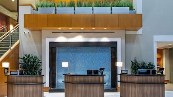 A hotel reception area with three wooden reception desks, a blue patterned wall, and a staircase on the left.