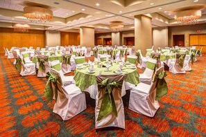 Een balzaal met ronde tafels klaar voor evenementen, met groen en witte tafelkleden en bijpassende stoerhoezen.