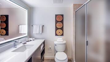 A modern bathroom with a white sink, mirror, and toilet. There are decorative wall art pieces above the toilet and a towel rack with white towels.