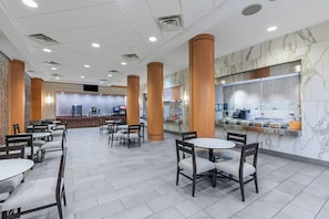 A modern hotel lobby with a marble reception desk, multiple seating areas, and a large window overlooking the interior.