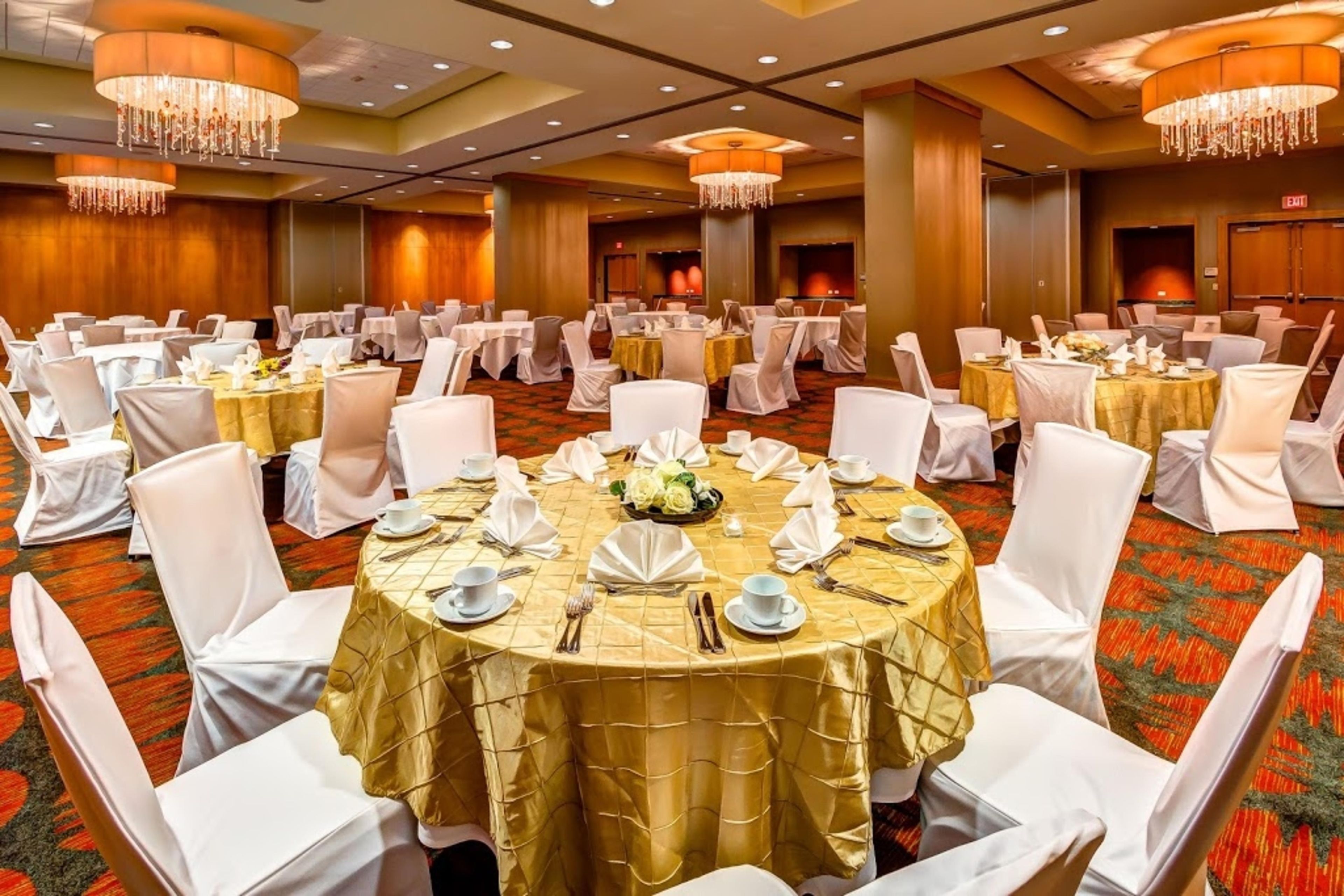 Un salón de banquetes con mesas redondas, sillas blancas y candelabros.