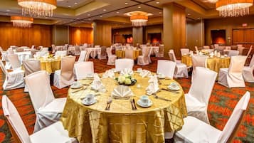 Un salón de banquetes con mesas redondas, sillas blancas y candelabros.