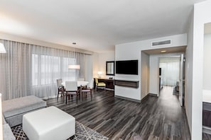 A hotel room with a dining area, a flat-screen TV mounted on the wall, and a modern design.