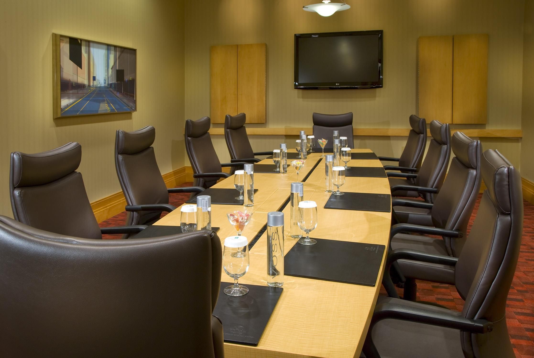 Une salle de conférence avec une longue table, des fauteuils en cuir noir et un téléviseur à écran plat fixé au mur.