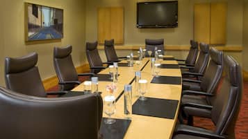 Un salón de conferencias con una larga mesa, sillas de cuero negro y un televisor de pantalla plana en la pared.