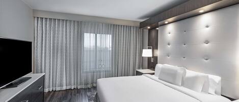 Une chambre d’hôtel moderne dotée d’un grand lit, d’un téléviseur à écran plat, d’une table de chevet et d’une fenêtre avec des rideaux.