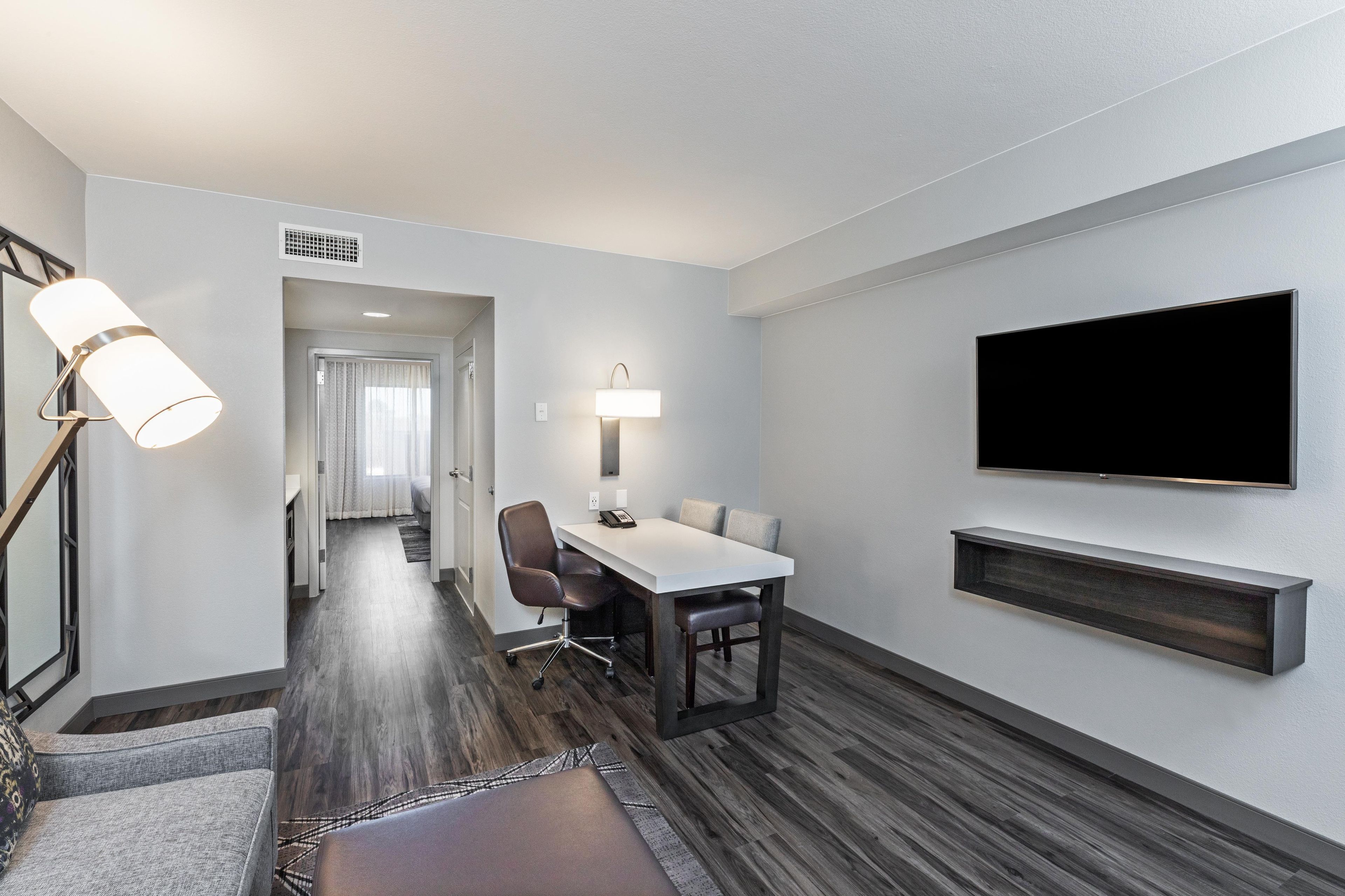 A hotel room with a dining area, a flat-screen TV mounted on the wall, and a modern lamp.