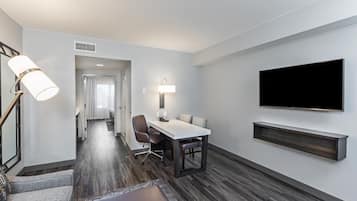 A hotel room with a dining area, a flat-screen TV mounted on the wall, and a modern lamp.
