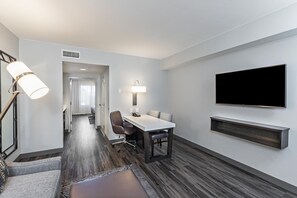 A hotel room with a dining area, a flat-screen TV mounted on the wall, and a modern lamp. - Embassy Suites by Hilton Houston Energy Corridor (Houston)