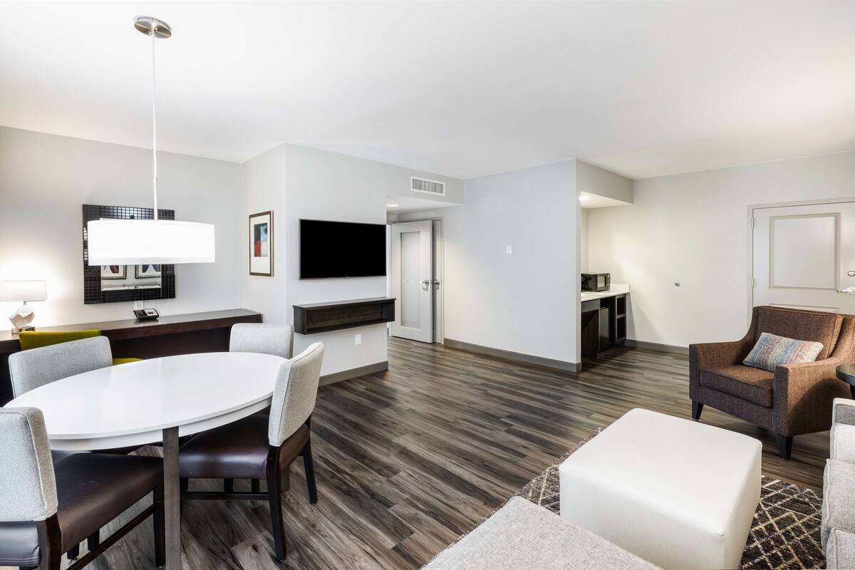 A modern living room with a round dining table, a sofa, and a TV mounted on the wall.