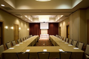 A conference room with a long table, chairs, a projector screen, and a stage area. - Embassy Suites by Hilton Houston Energy Corridor (Houston)