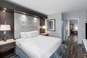 Een hotelkamer met een groot bed, bedlampen, een nachtkastje, een kunstwerk in een lijst en uitzicht op de gang.
