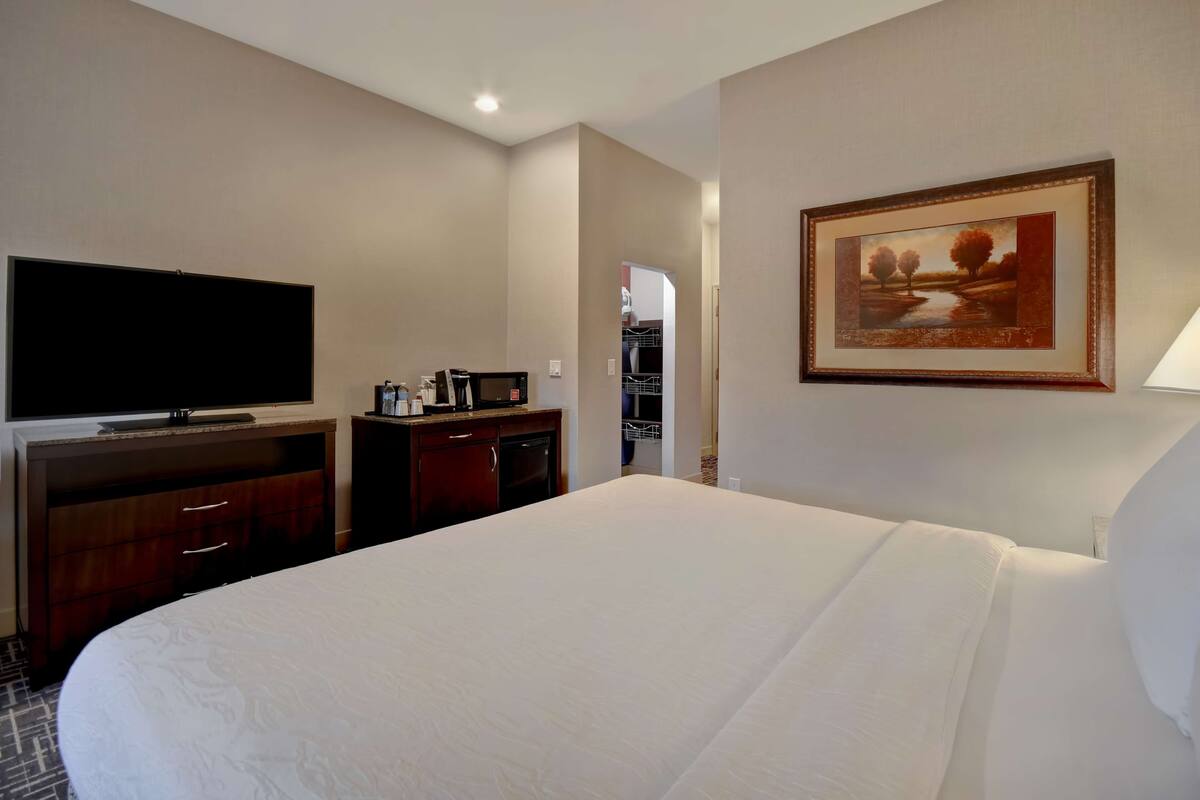 A hotel room with a large bed, a flat-screen TV, a microwave, and a painting on the wall.