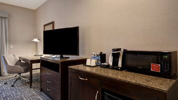 A hotel room with a desk, a flat-screen TV, a microwave, a coffee maker, and a mini-fridge.
