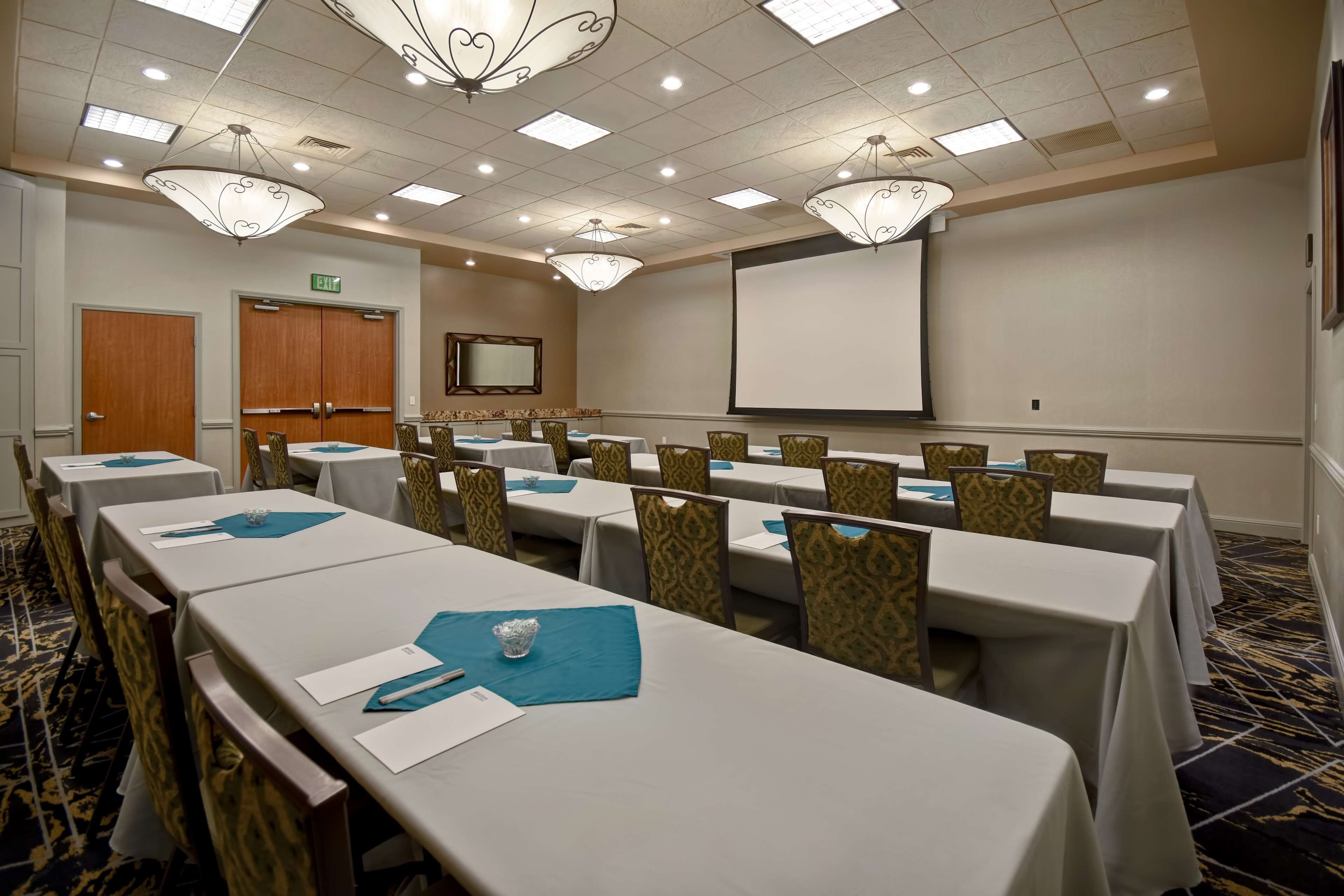 A conference room with long tables, chairs, and a projector screen.