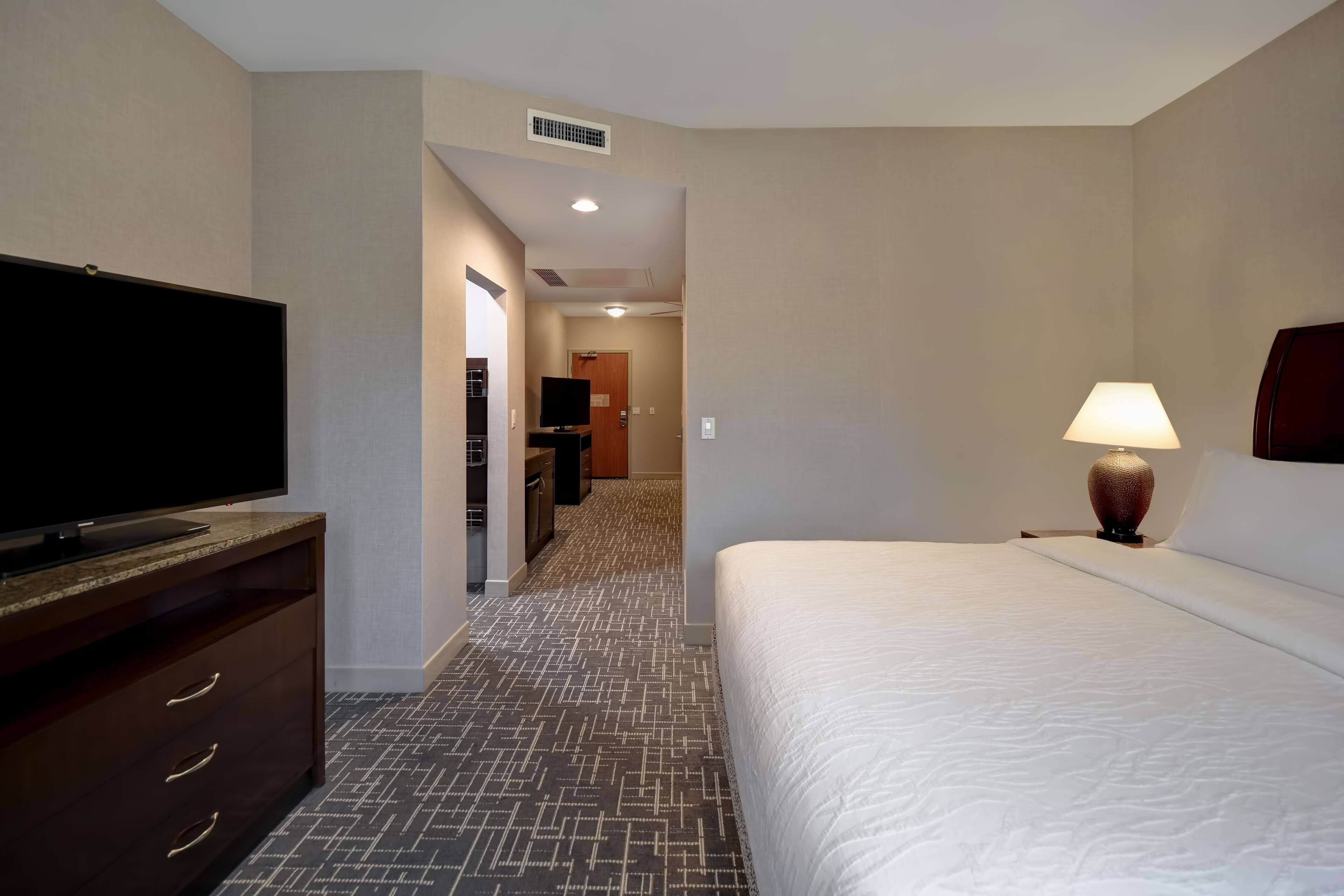 Een hotelkamer met een bed, een televisie op een dressoir, een lamp en een gang naar een badkamer.