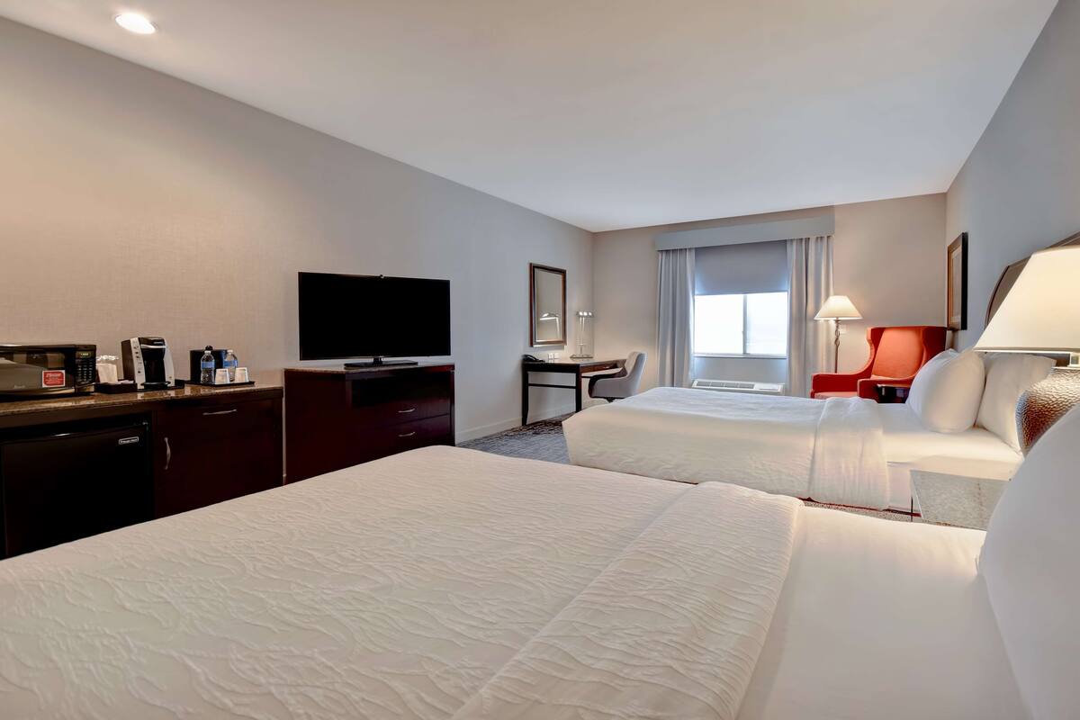 A hotel room with two beds, a desk, a television, and a desk lamp.