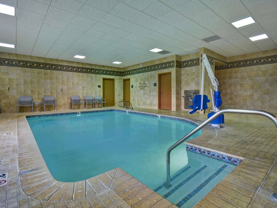 Una piscina interior con paredes de azulejos, una escalera de piscina y algunas sillas cerca.